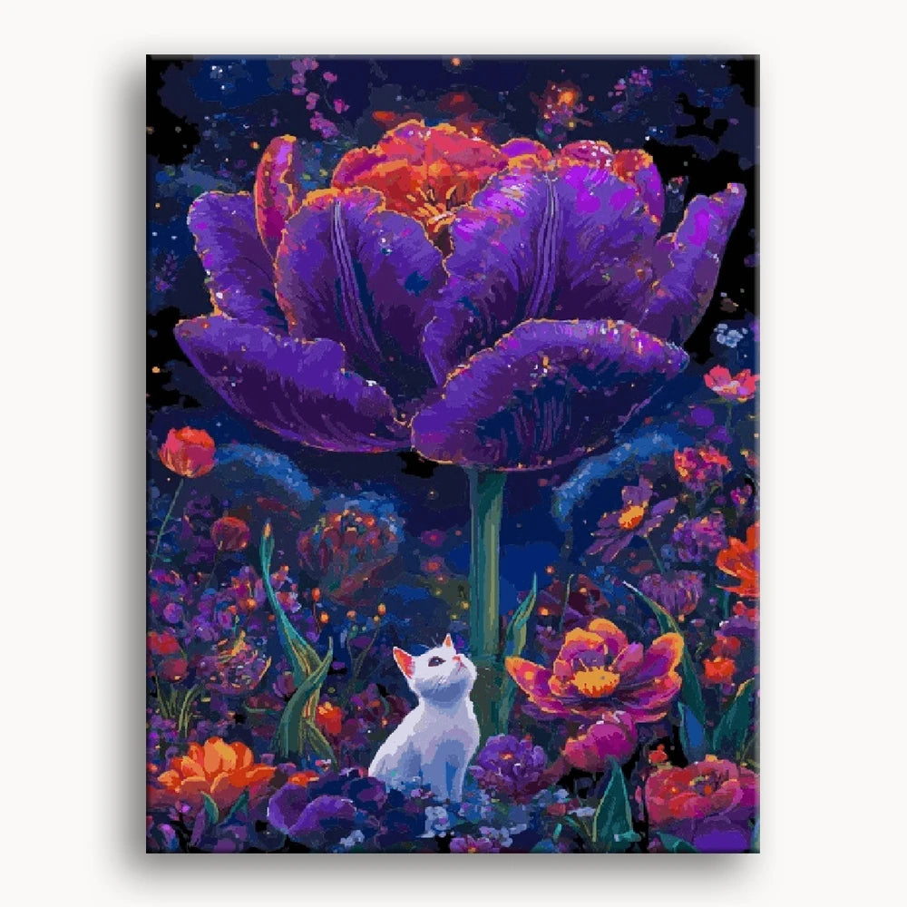 A playful cat sits beside a vibrant purple flower in a sunny field, surrounded by green grass.